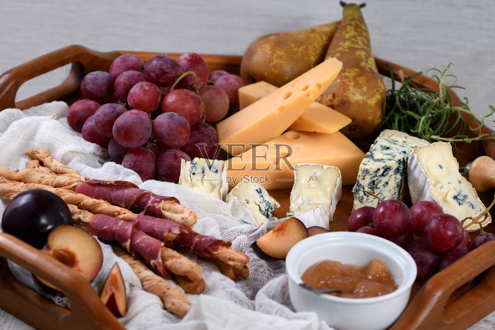 开胃菜。脆脆的grissini包在晒干的培根，布里干酪片，卡门贝尔奶酪，蓝奶酪，雷默尔和麝香葡萄藤与水果。照片摄影图片