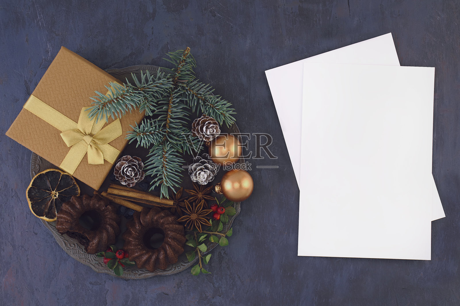 圣诞节的心情。礼物有玩具，巧克力松饼，香料，云杉树枝和浆果在一个金属复古盘子，银勺子，一杯咖啡和肉桂在桌子上。俯视图照片摄影图片