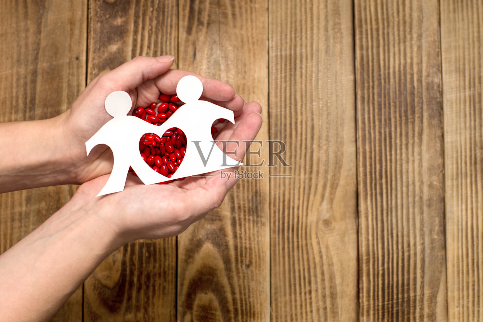 情侣们被剪成纸片，放在木头背景上。这颗心是在一张纸上剪下来的，背景是鲜红的barberry浆果。情人节照片摄影图片