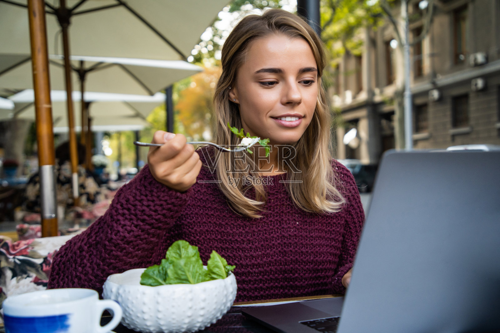 年轻女子坐在街边的咖啡馆里用笔记本电脑享用沙拉照片摄影图片