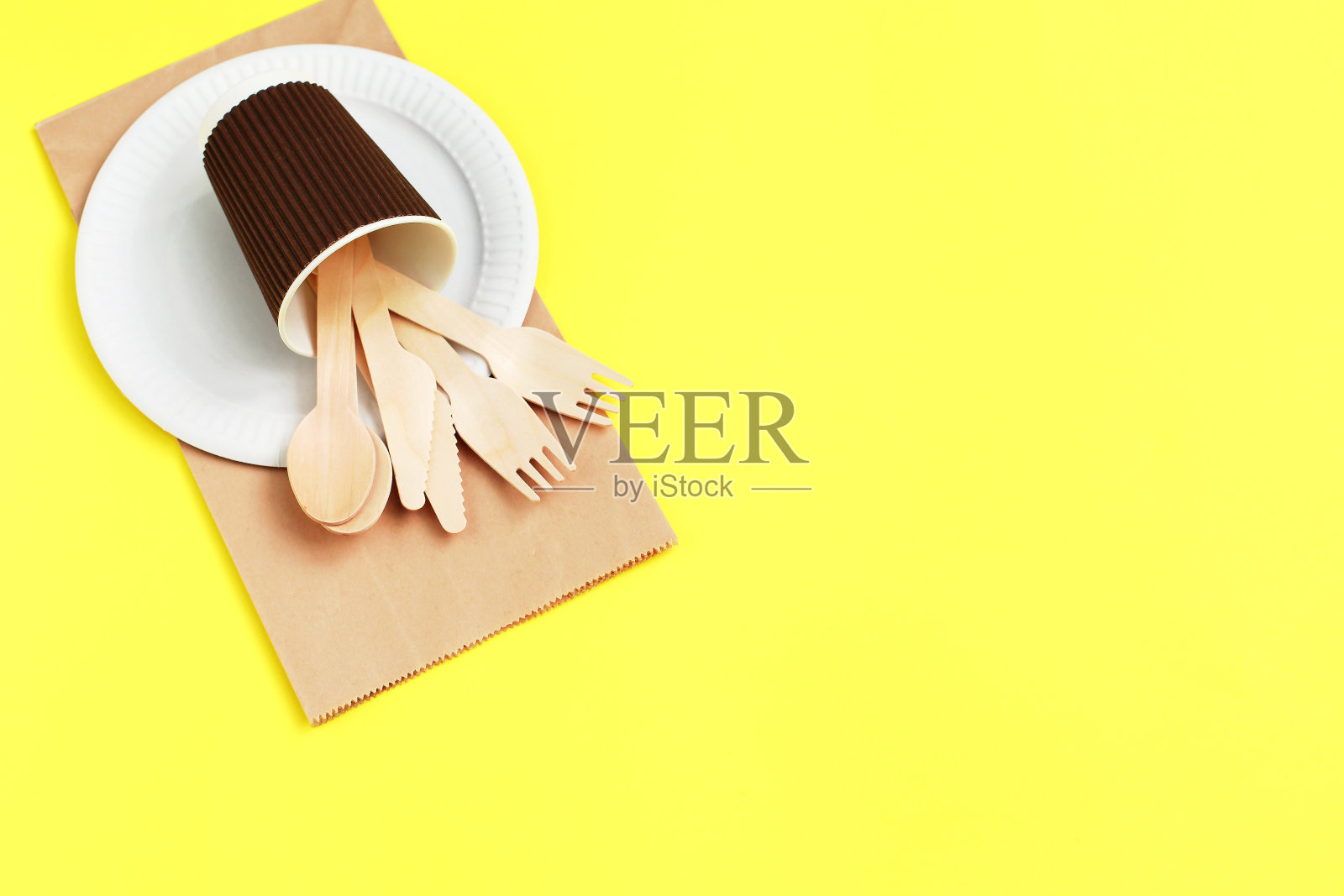 用竹木制成的环保一次性用具，包装在纸袋上，背景为黄色。照片摄影图片