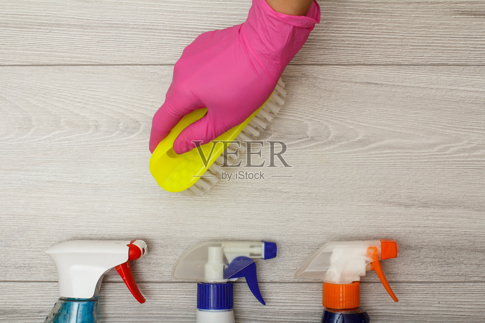 手握橡胶手套，用刷子将装有洗涤剂的瓶子放在木制背景上。照片摄影图片