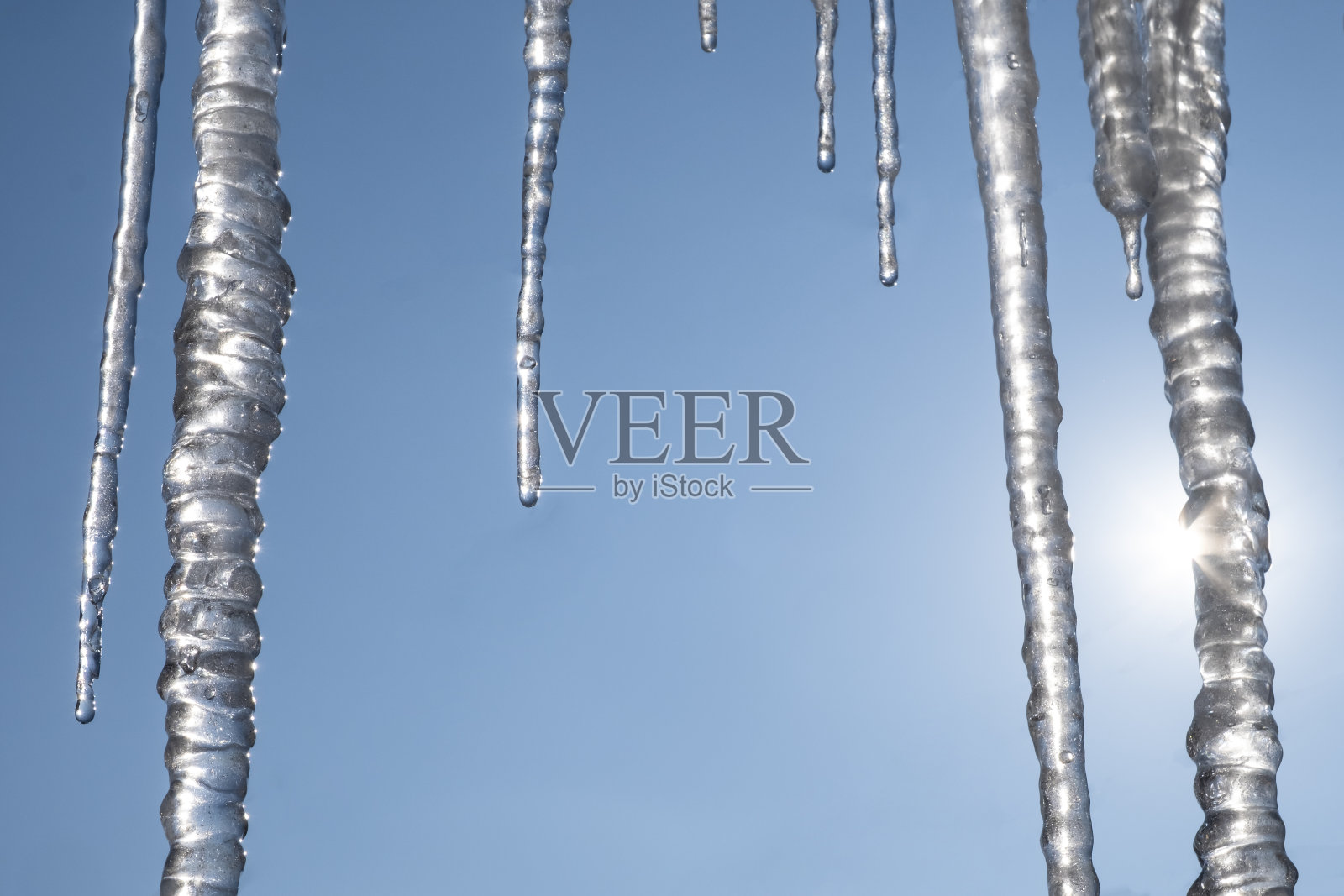 屋顶上挂着冰柱，背景是晴朗的蓝天和阳光。照片摄影图片