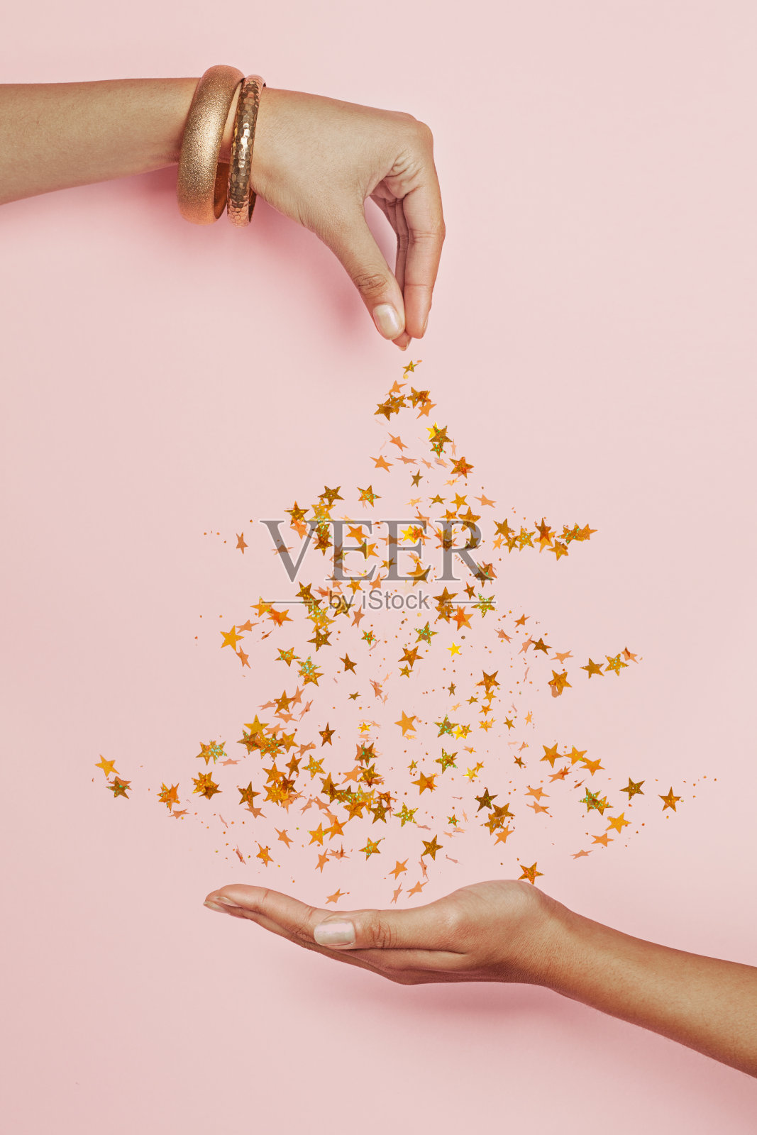 这棵圣诞树是用粉红色背景上的金色星星和黑色女人的手做成的。简易圣诞卡构图照片摄影图片