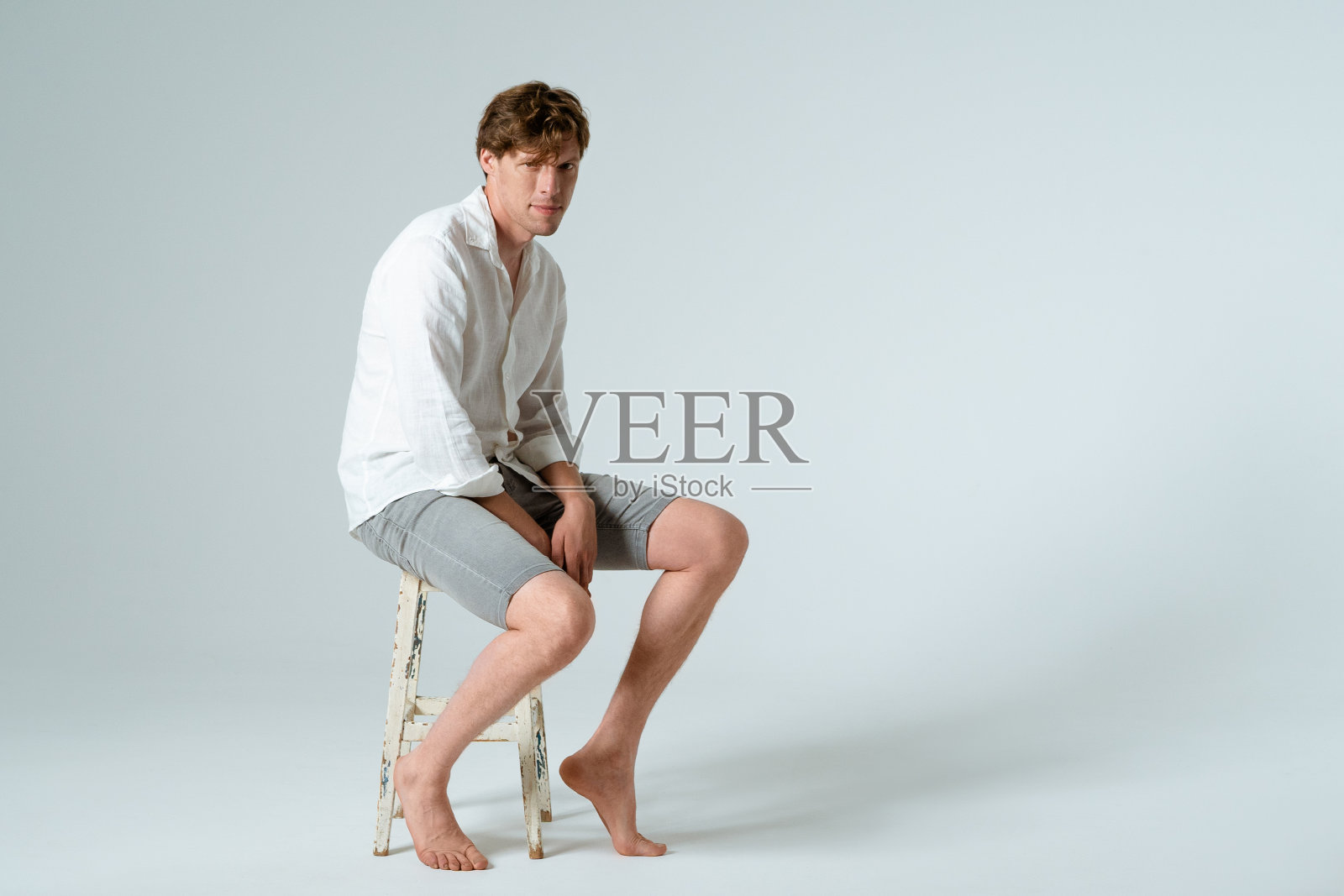 年轻男子的肖像全长坐在椅子上，看着相机孤立的白色背景。本空间照片摄影图片