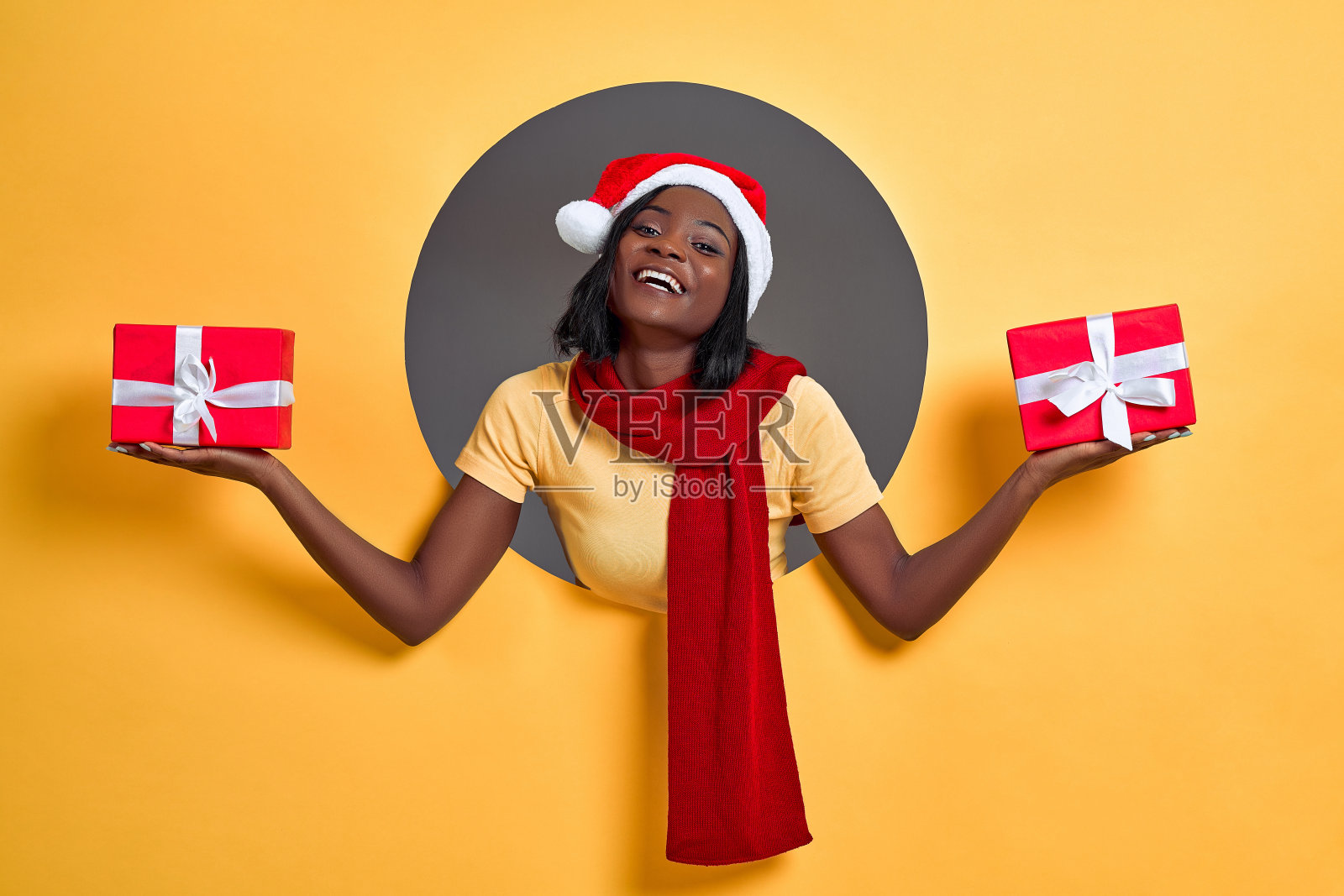 圣诞黑人妇女手里拿着两个礼品盒，黄色背景下孤立的圆圈。圣诞礼物的概念。照片摄影图片