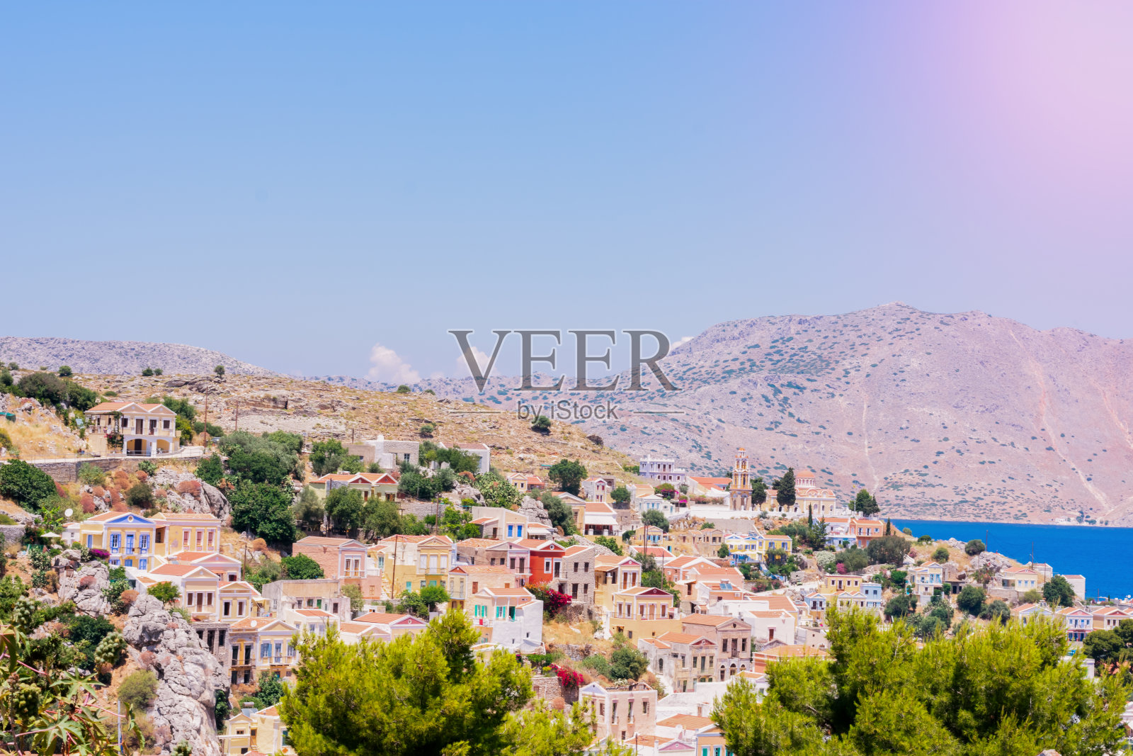 风景如画的岩石上五颜六色的小房子，地中海附近的希腊岛上的绿树在阳光明媚的夏日，在异国情调的岛屿上度假照片摄影图片