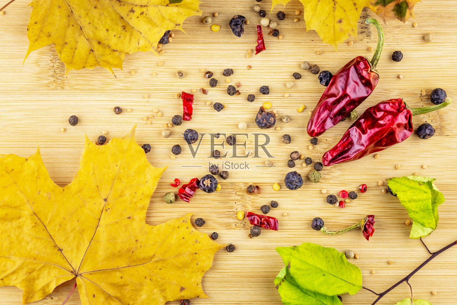 切菜板上放着两个红辣椒和几种香料(芥末、杜松)。背景是一片黄色的枫叶照片摄影图片