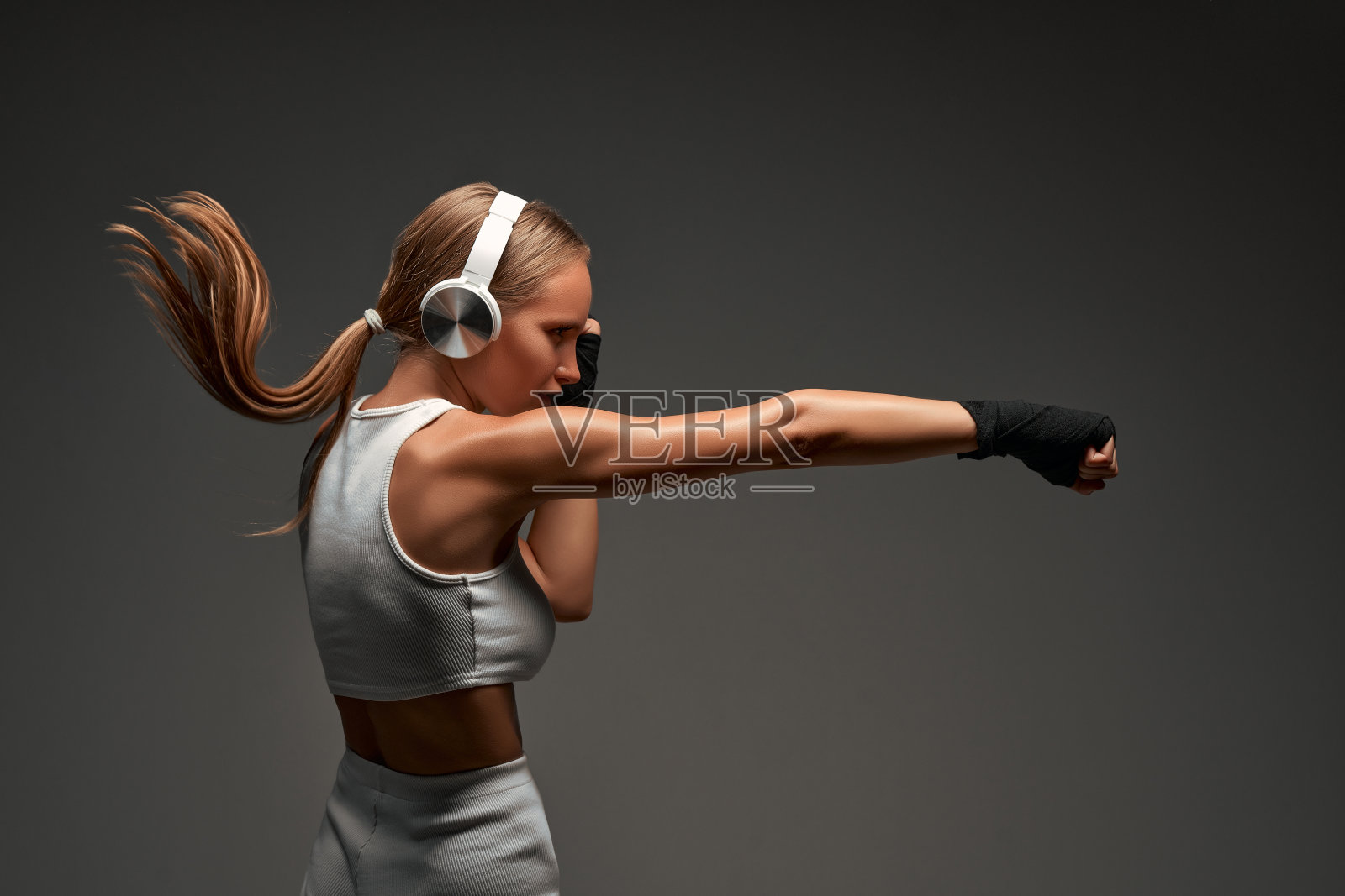 运动女拳击手与耳机灰色背景。照片摄影图片