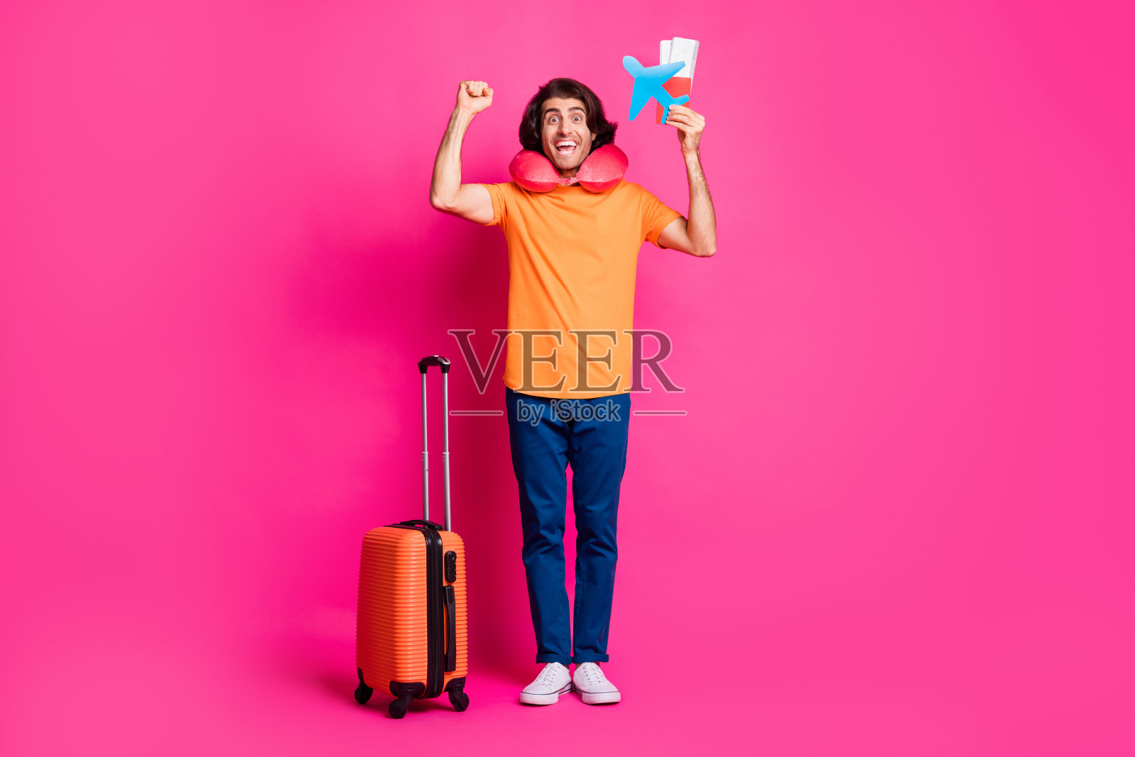 全长照片的家伙行李票纸飞机举起拳头穿颈部坐垫橙色t恤牛仔裤运动鞋孤立亮粉色背景照片摄影图片