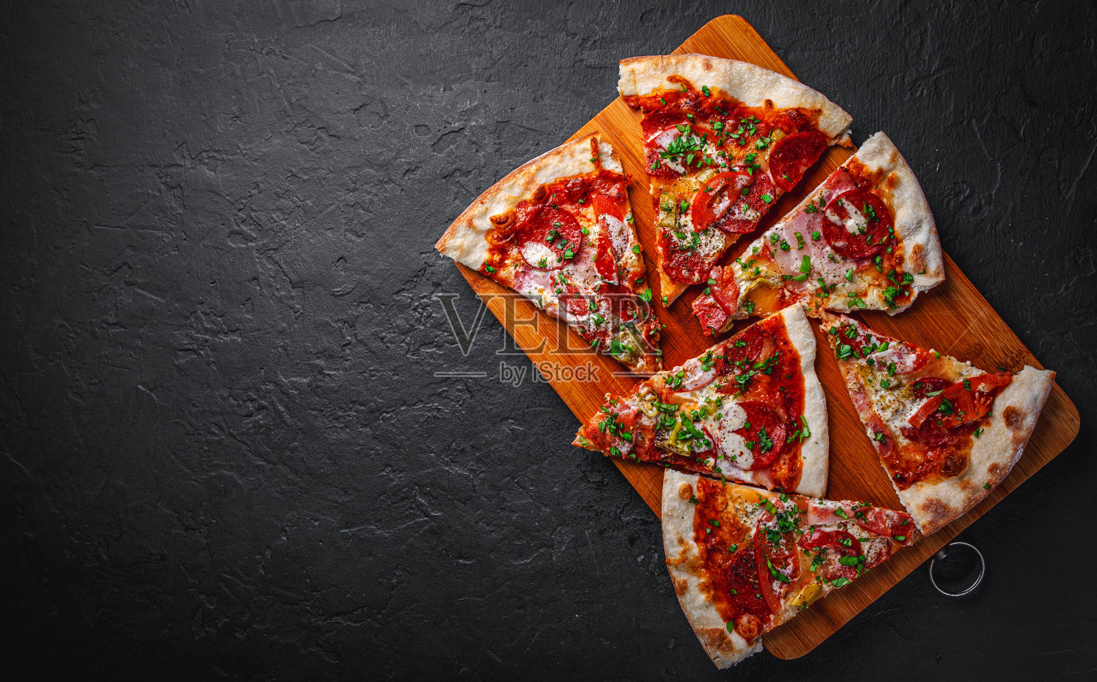 披萨切片配马苏里拉芝士，火腿，番茄酱，辣椒，意大利腊肠。意大利披萨在深灰色的黑色石板背景照片摄影图片