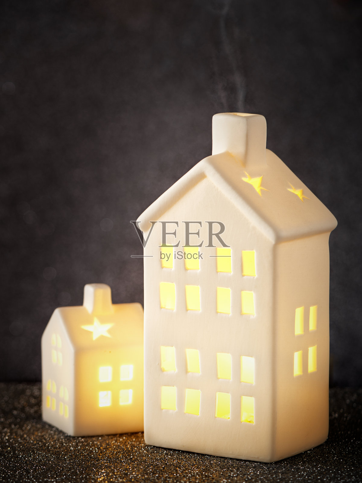 两个白色的陶瓷房子，窗户上有灯光，烟囱里有烟，在黑暗和明亮的背景下，复制空间极简主义，选择性的焦点。照片摄影图片