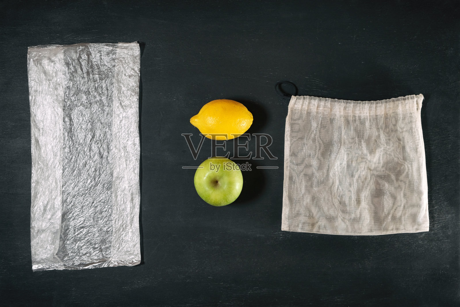 新鲜的绿苹果和黄柠檬在一次性塑料包装和时髦的可重复使用的生态杂货网之间的比较，有意识的消费主义概念，可持续的生活环境污染照片摄影图片