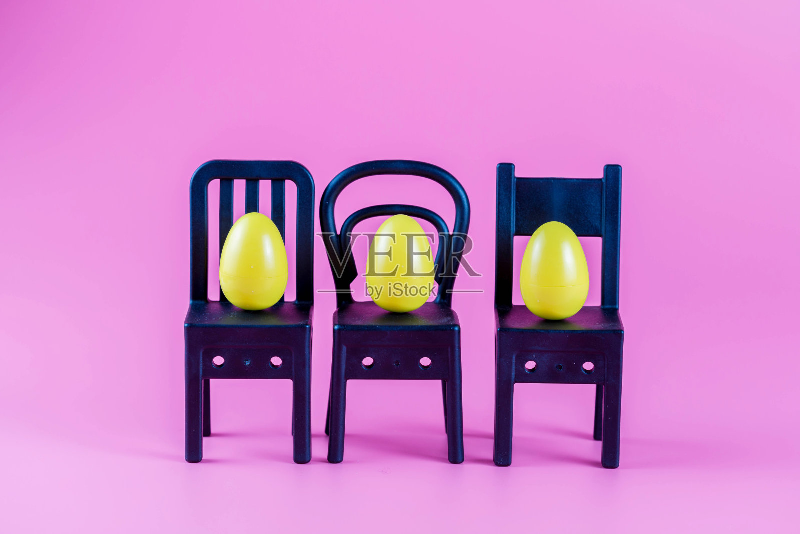 粉红色背景的小椅子上放着五颜六色的塑料复活节彩蛋。照片摄影图片
