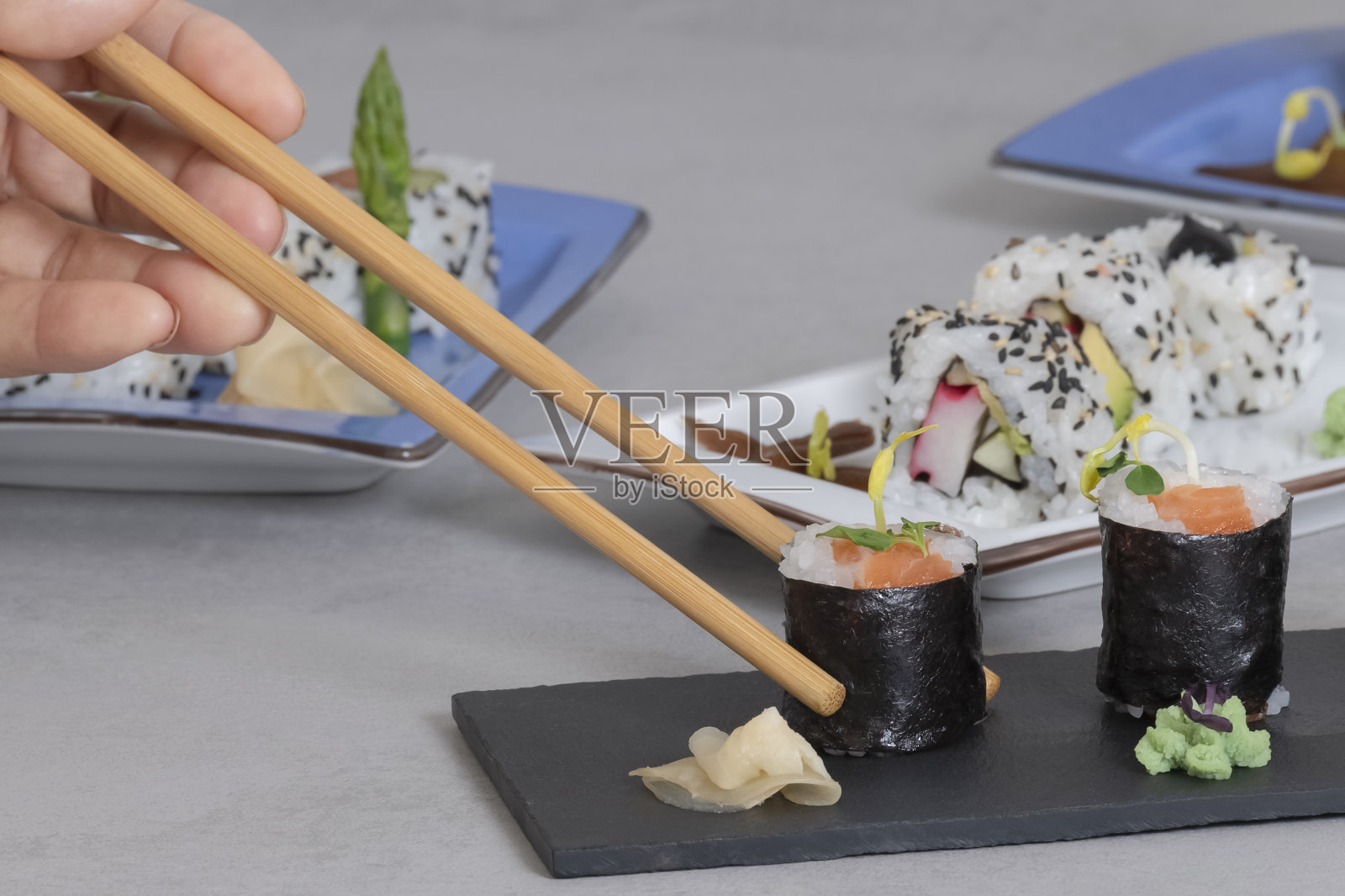 近距离的筷子拿起一个美味的看起来maki从盘子周围的焦点盘子寿司。寿司与健康食品的概念。照片摄影图片