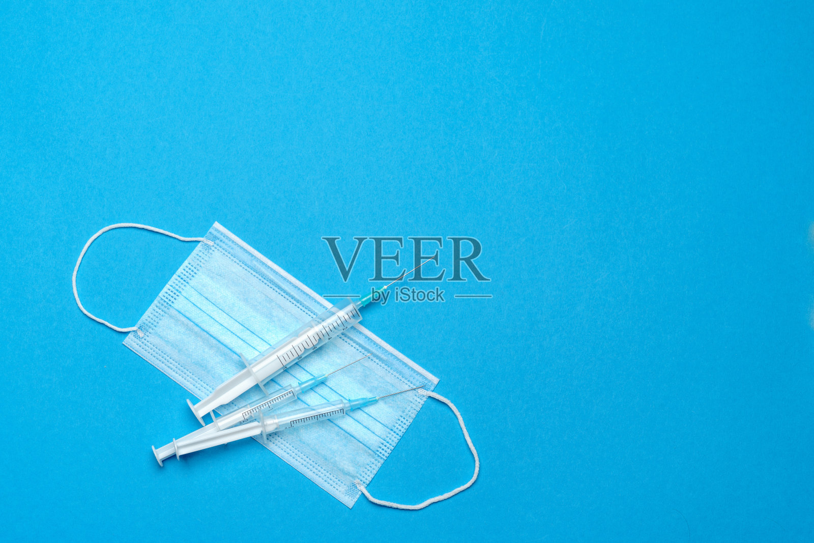 预防COVID-19病毒的注射器和一次性口罩，蓝色背景照片摄影图片