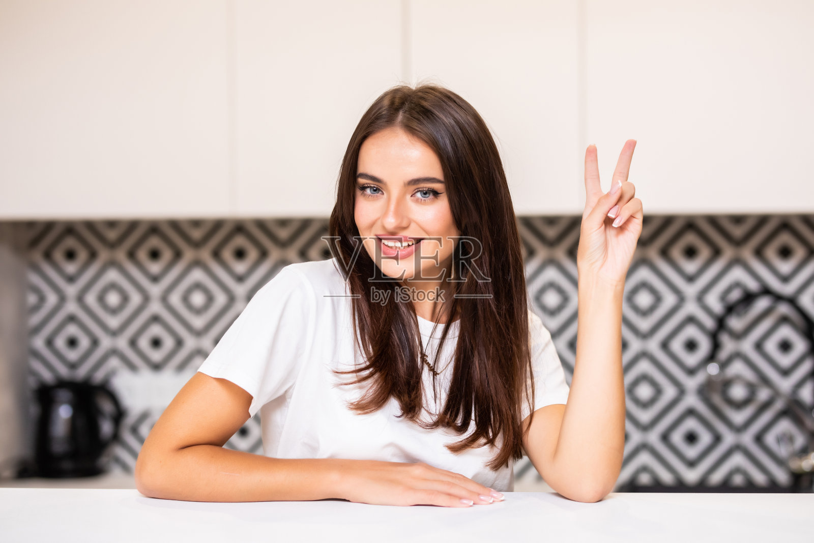 在明亮的厨房里，一位美女坐在餐桌前做着和平手势照片摄影图片