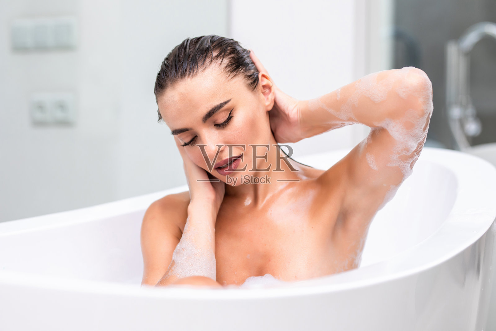 近距离热辣的女人躺在泡沫在浴室。性感女人放松在豪华浴缸。照片摄影图片