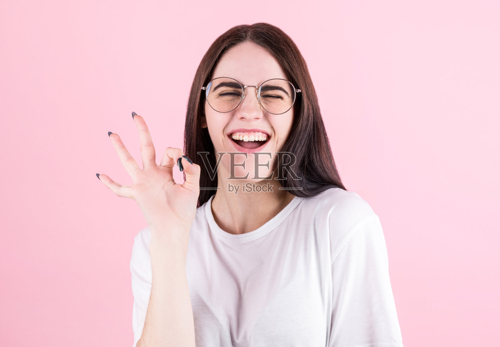 长黑发的女孩眨着眼睛，微笑着，表现出OK的迹象。富有表现力的面部表情照片摄影图片