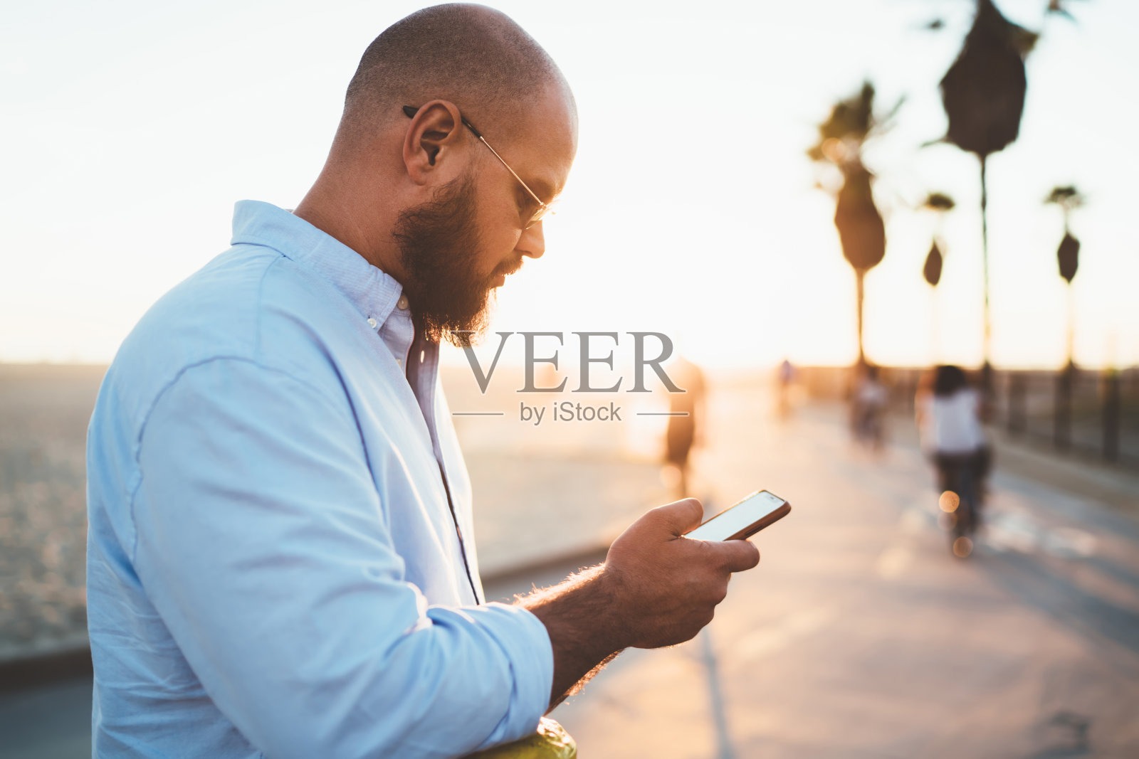 留着胡子的年轻男性拿着智能手机浏览关于咖啡馆的信息，在街上消磨时间，帅气的潮男在空闲时间用手机在社交网络上观看在线视频照片摄影图片