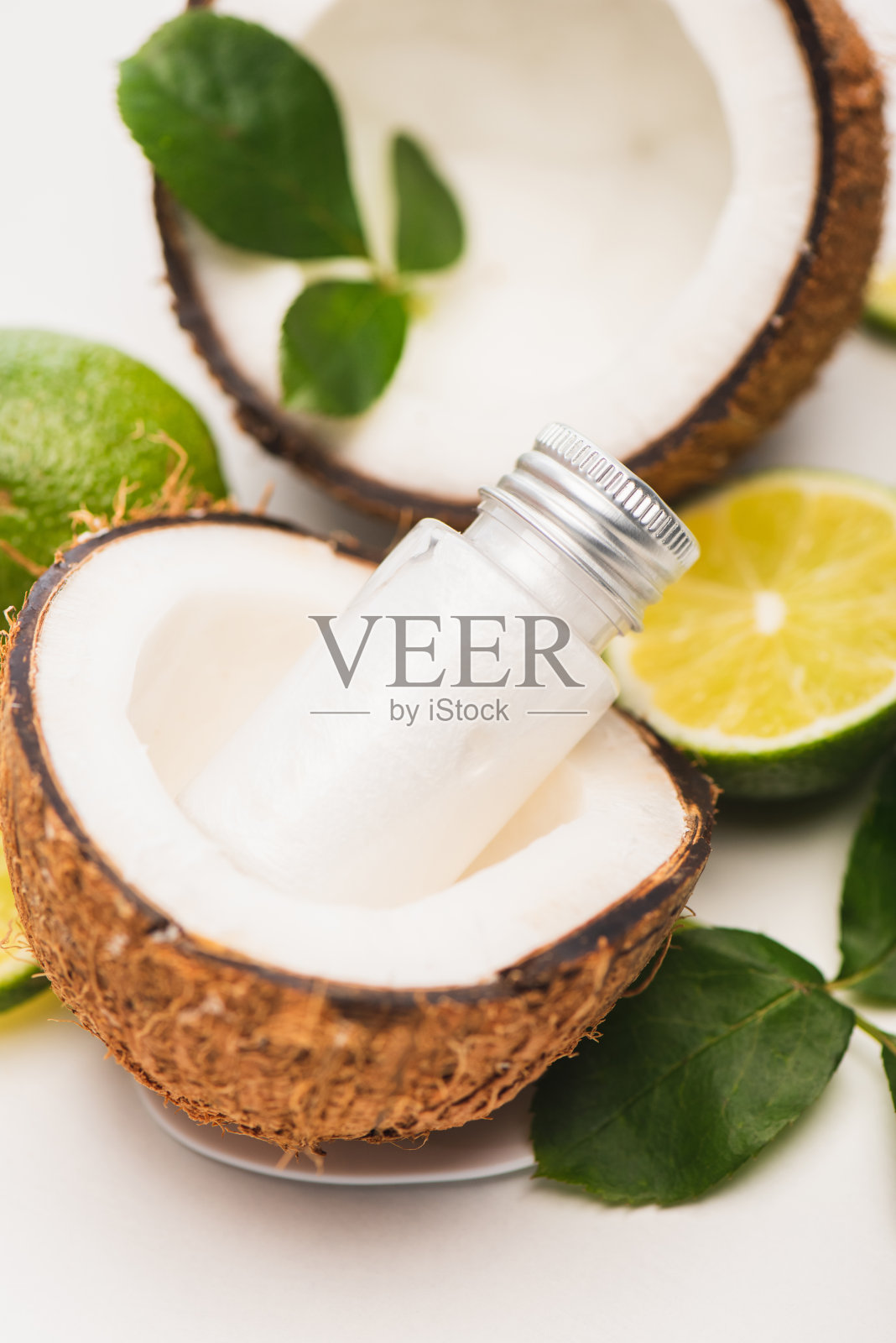 瓶子的洗液在椰子近一半的酸橙，和玫瑰叶在模糊的白色背景照片摄影图片