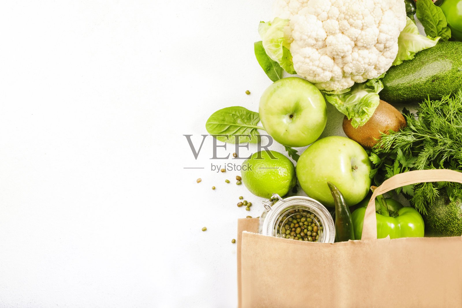 绿色素食在全纸质购物袋，蔬菜和水果在白色的背景。超市购物，生食和清洁饮食理念。健康的食物照片摄影图片