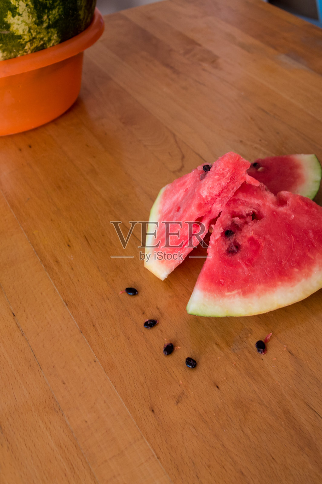 木桌上放着几片成熟的西瓜和瓜子。照片摄影图片