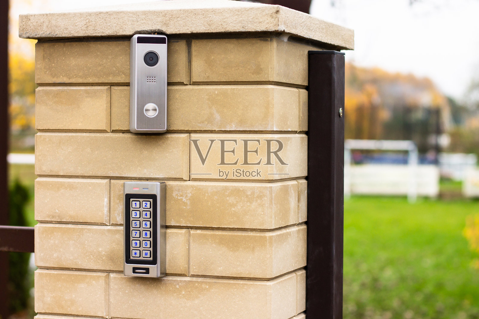 银色对讲机呼叫面板，蓝色数字按钮和一个摄像机在一个私人住宅的砖米色篱笆柱上照片摄影图片