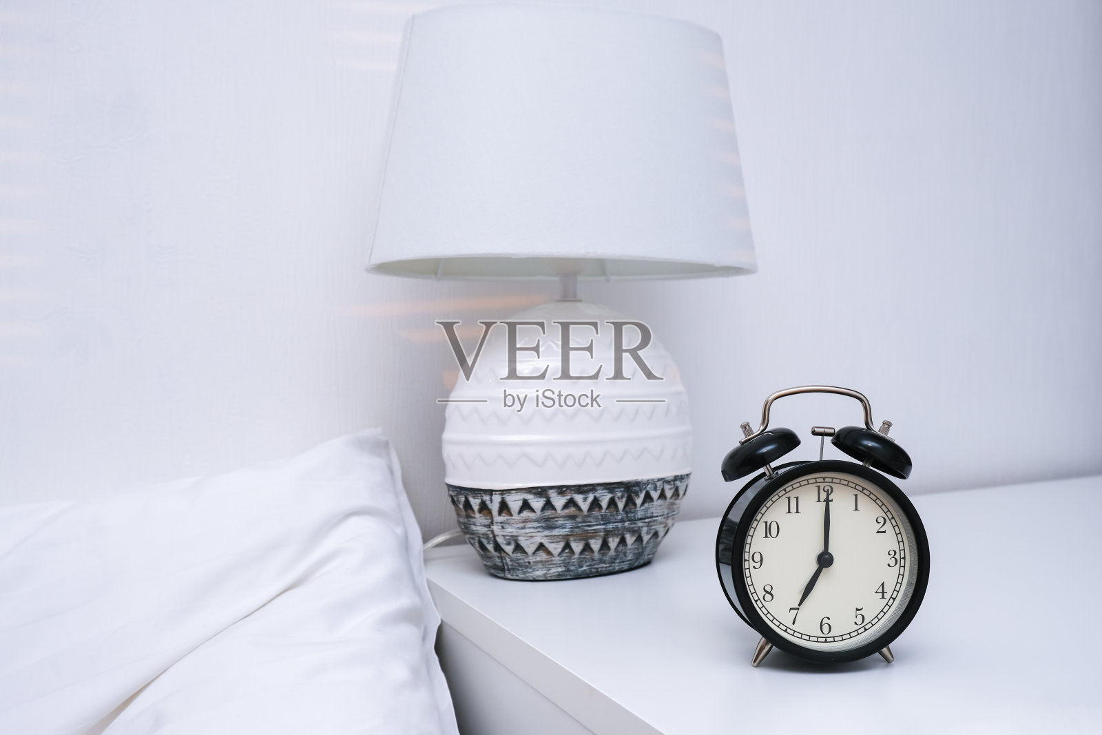 一个显示早上7点的闹钟放在床边的桌子上，上面有灯照片摄影图片