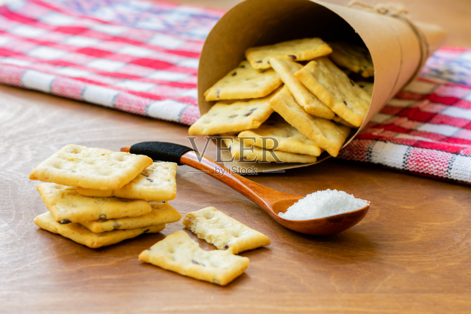 咸脆饼干，木勺里放着盐晶，木桌上放着红色餐巾，上面放着装满饼干的纸袋照片摄影图片