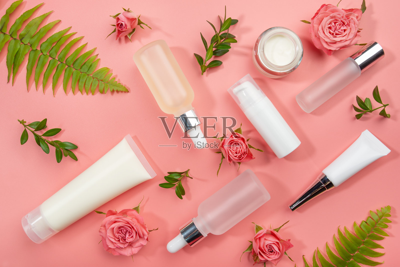 平铺化妆品瓶和容器与玫瑰和绿色蕨叶在粉红色的背景照片摄影图片