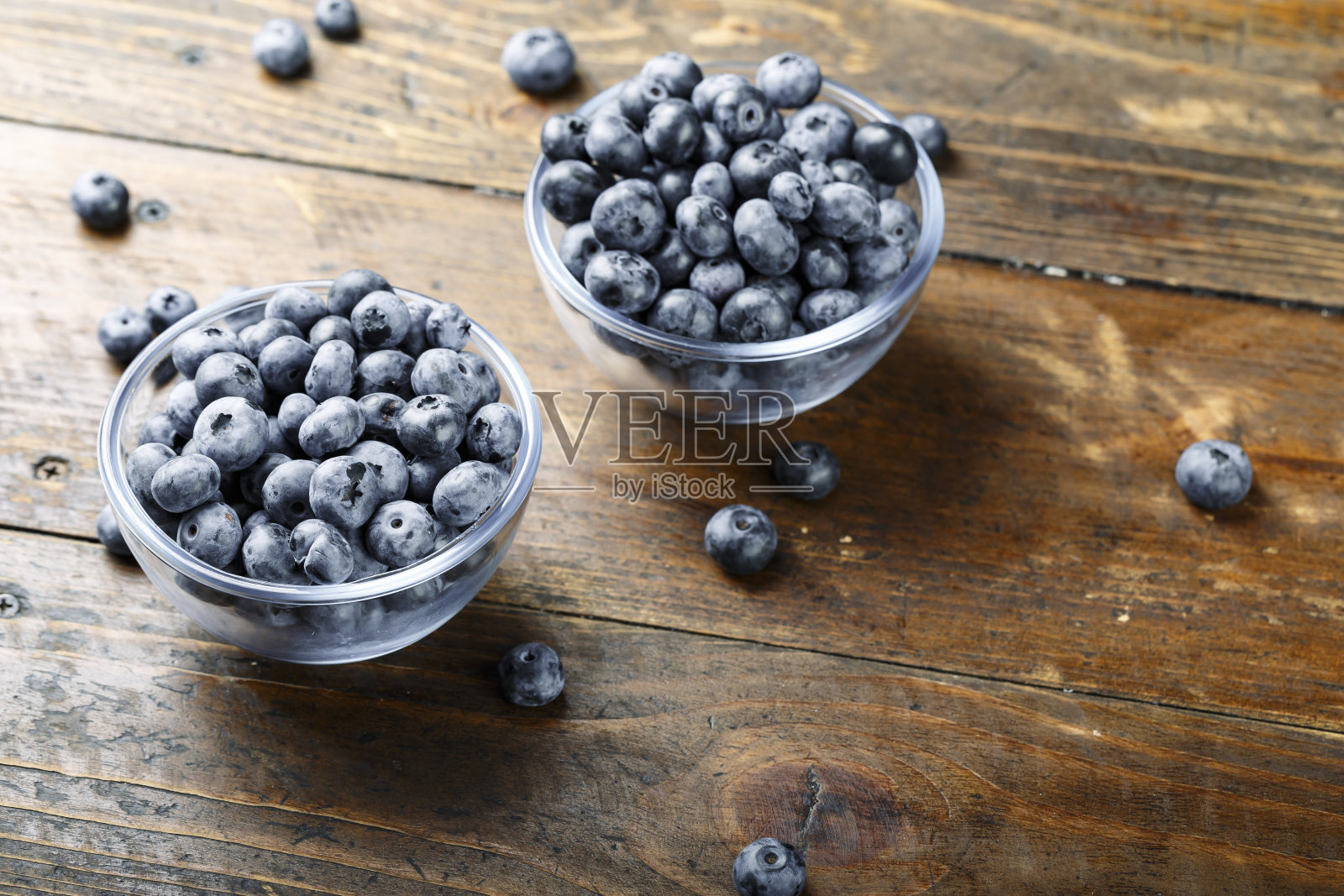 新鲜的蓝莓放在一个玻璃碗里，散落在一张木桌上。食物含有抗氧化剂。照片摄影图片
