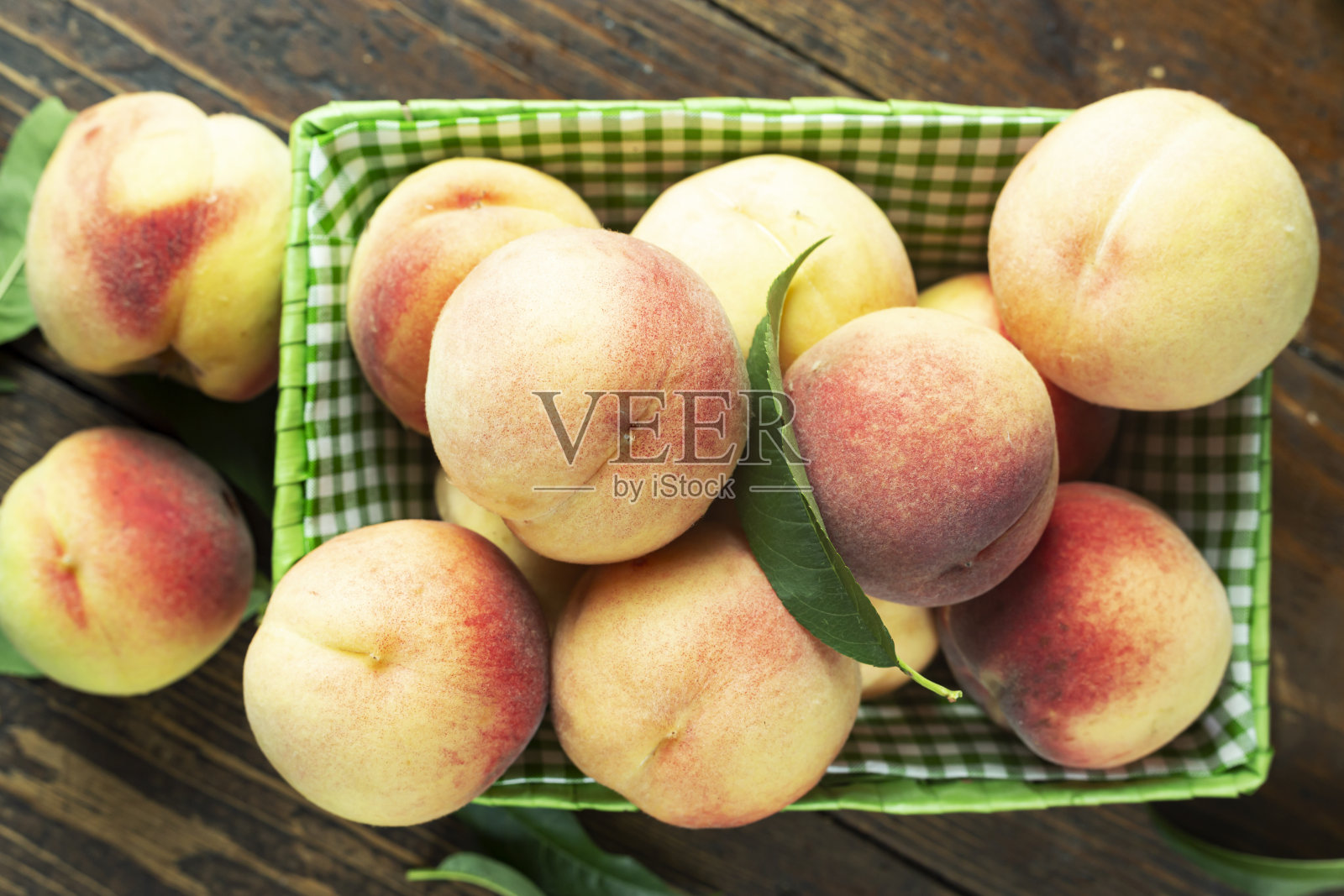 新鲜收获的桃子装在一个篮子里放在一个木制的乡村桌子上。桃叶存在于成分中。照片摄影图片