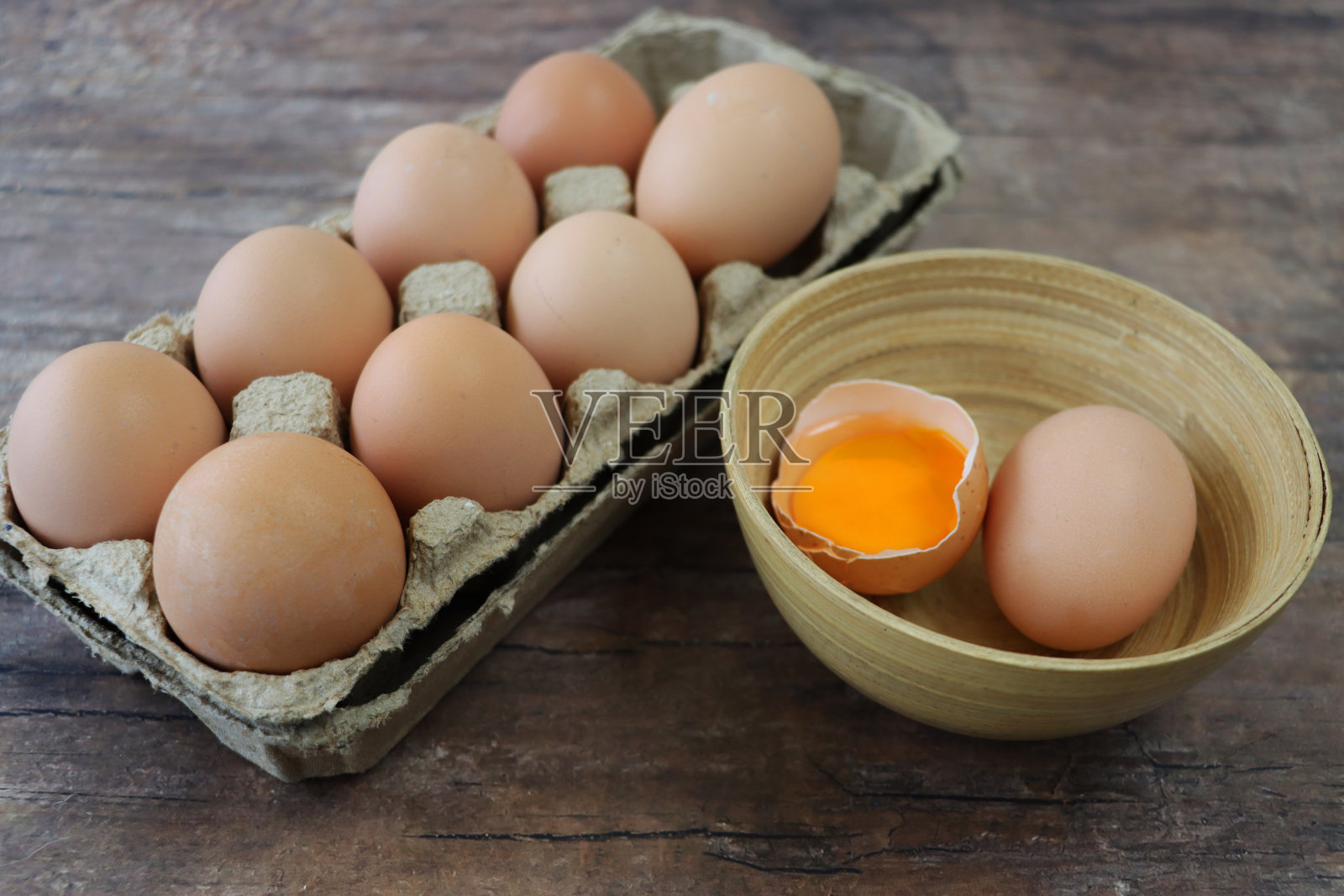 打开的图像，棕色纸板，鸡蛋盒，在木制的桌子上，包含一批棕色鸡蛋旁边的碗包含鸡蛋一个破碎显示蛋黄，工作室拍摄照片摄影图片