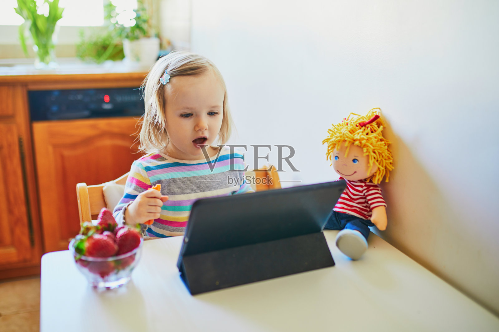 可爱的蹒跚学步的小女孩吃新鲜草莓和使用药片照片摄影图片