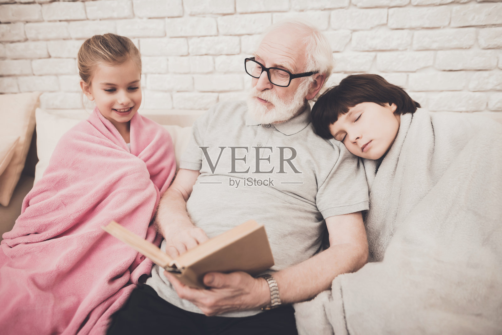 爷爷、孙子、孙女在家。爷爷正在给孩子们读书。照片摄影图片