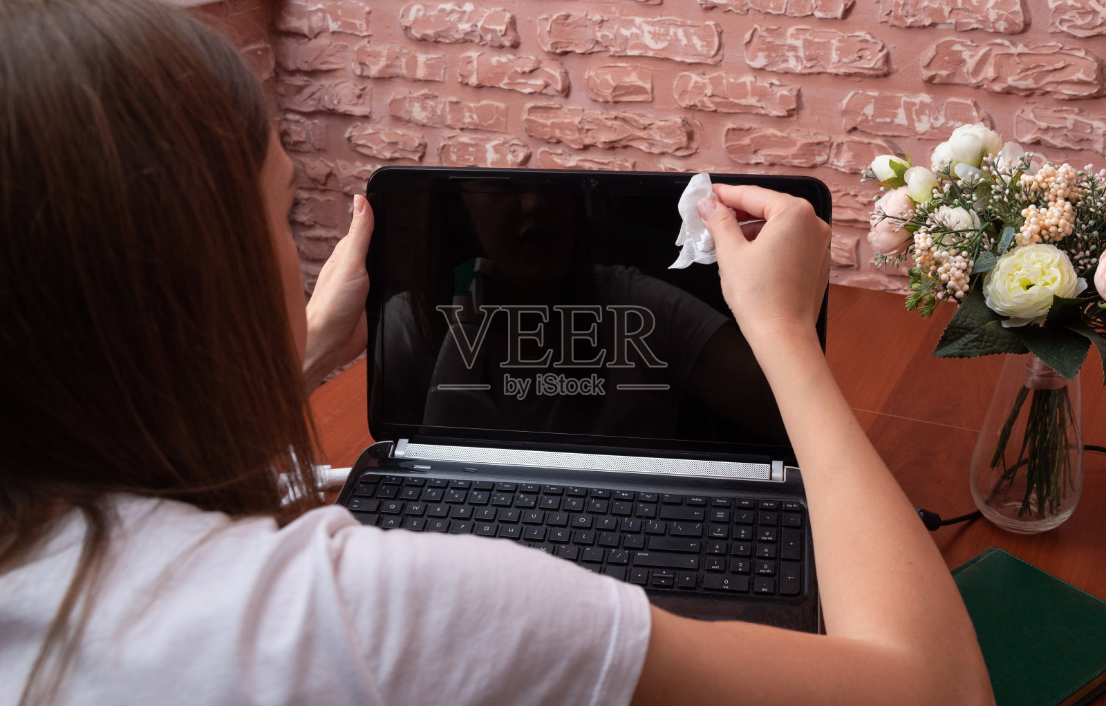 女孩用餐巾擦了擦笔记本电脑的屏幕。清理自由职业者工作场所的过程。照片摄影图片