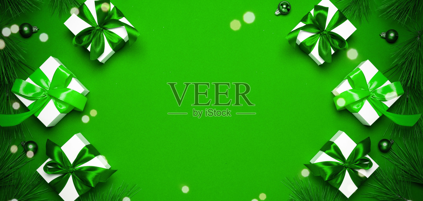 圣诞节销售。白色礼物与祖母绿颜色的蝴蝶结，绿色的球和闪闪发光的灯在绿色背景的圣诞装饰贺卡。文本的装饰和复制空间。照片摄影图片