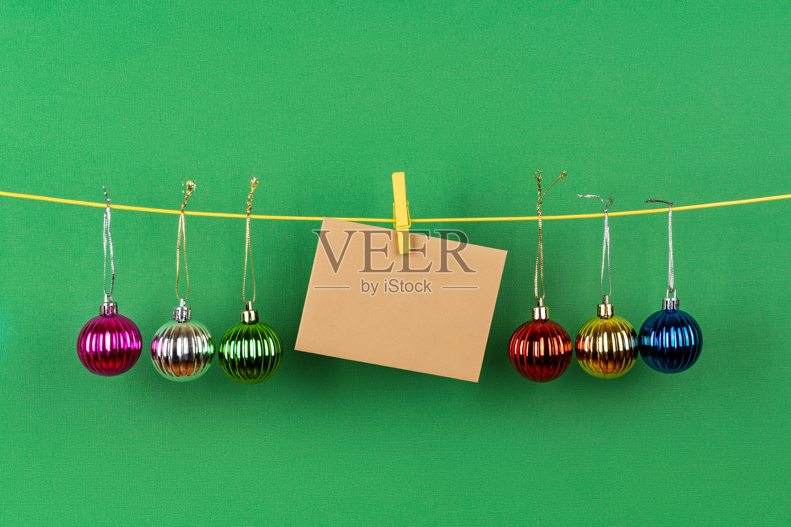 五颜六色的圣诞球和空白的棕色贺卡在绿色的背景下挂在绳子上。冬季有圣诞节和新年。副本的空间。照片摄影图片