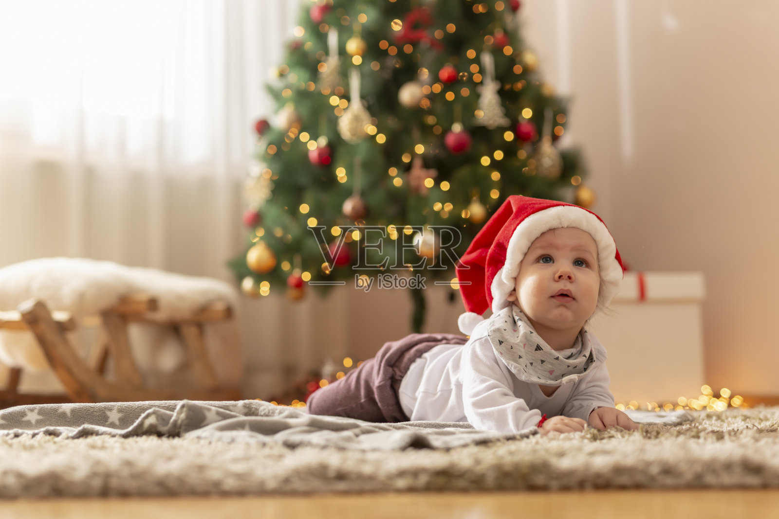 戴着圣诞帽的小男孩躺在圣诞树旁照片摄影图片