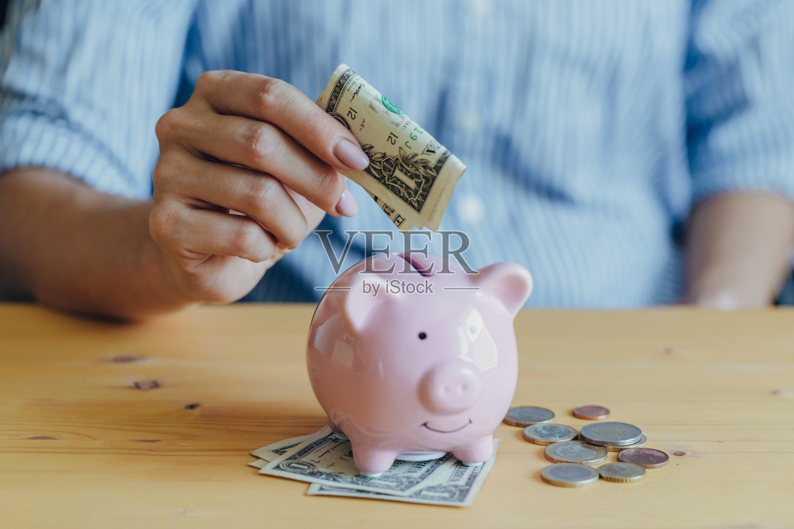 女人的手把一张纸币放在桌子上的一个粉红色的储蓄罐里。在全球危机中存钱或储蓄、投资的概念照片摄影图片