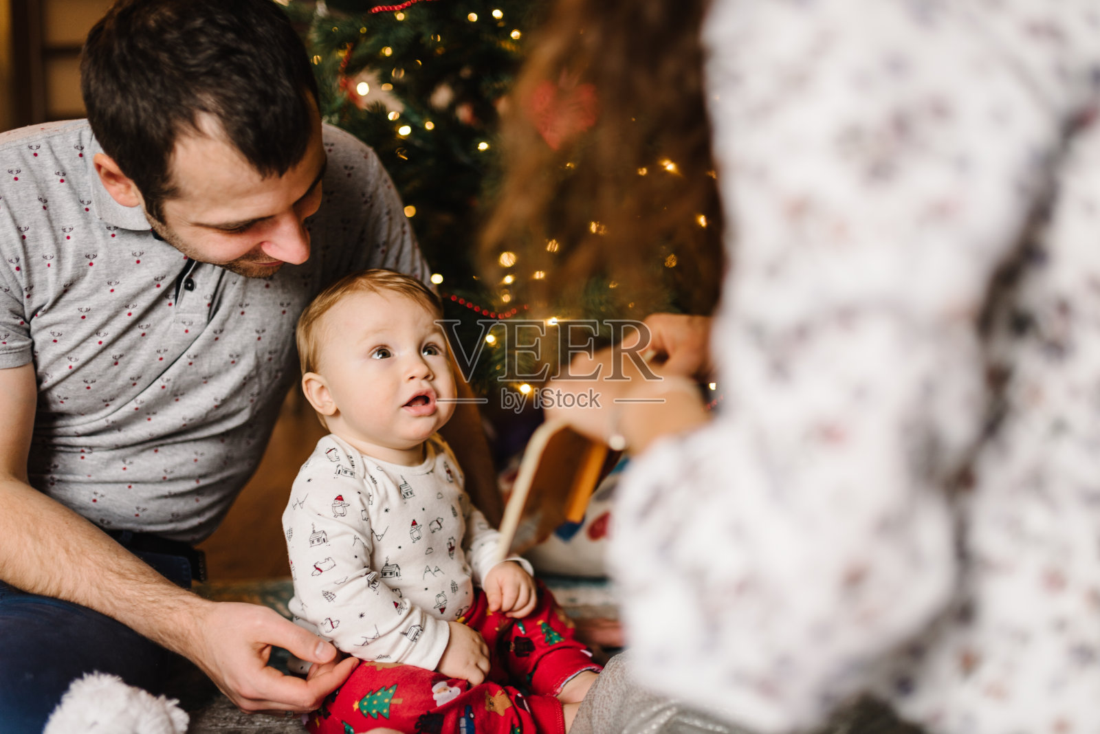 爸爸妈妈和小儿子在圣诞树旁玩玩具，新年快乐，圣诞快乐，圣诞装饰的室内，家庭节日概念照片摄影图片