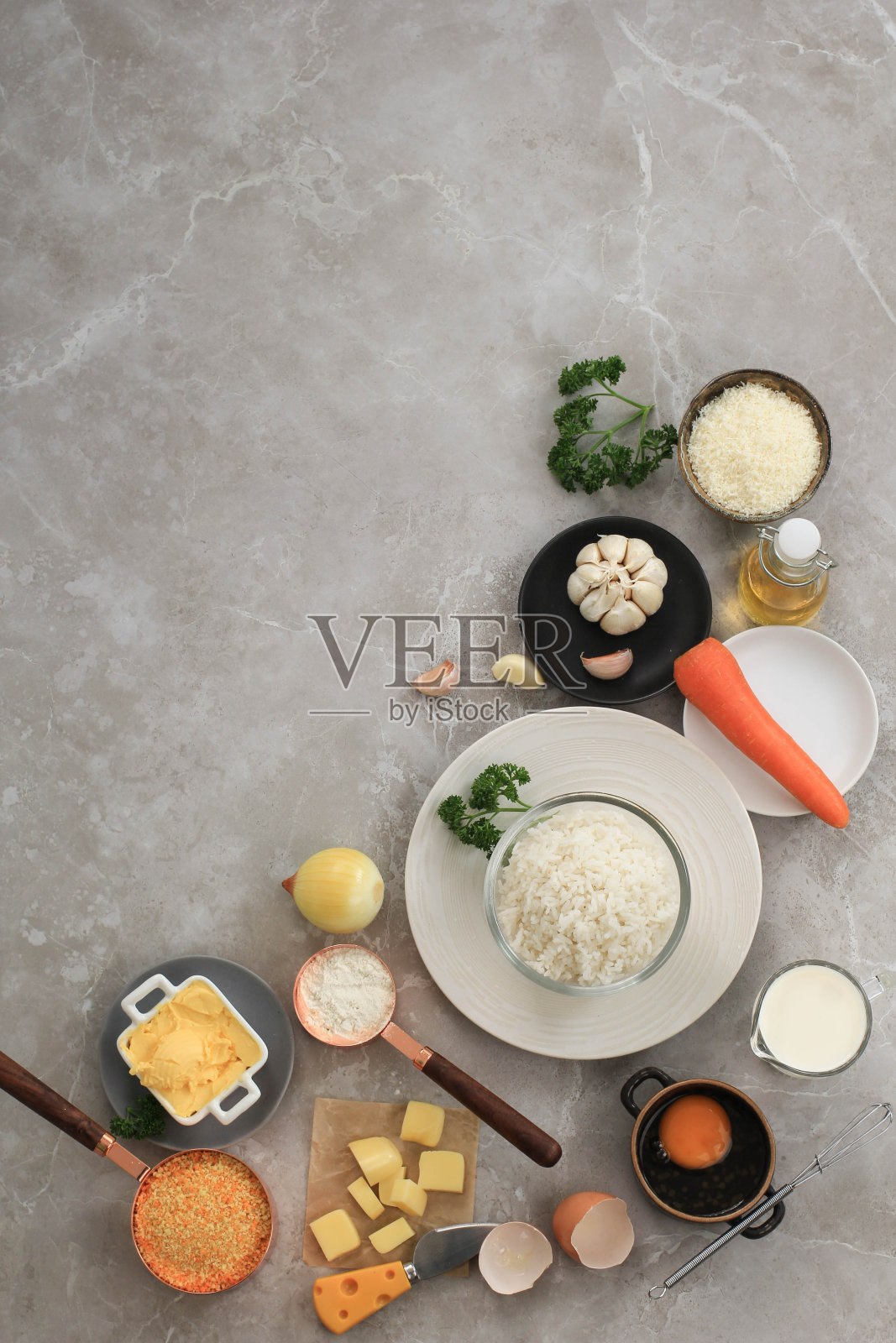 在白色灰色大理石背景上烹饪兰西尼的配料。奶酪，米饭，牛奶，鸡蛋，胡萝卜，欧芹，黄油，大蒜，面包屑，帕尔马干酪照片摄影图片