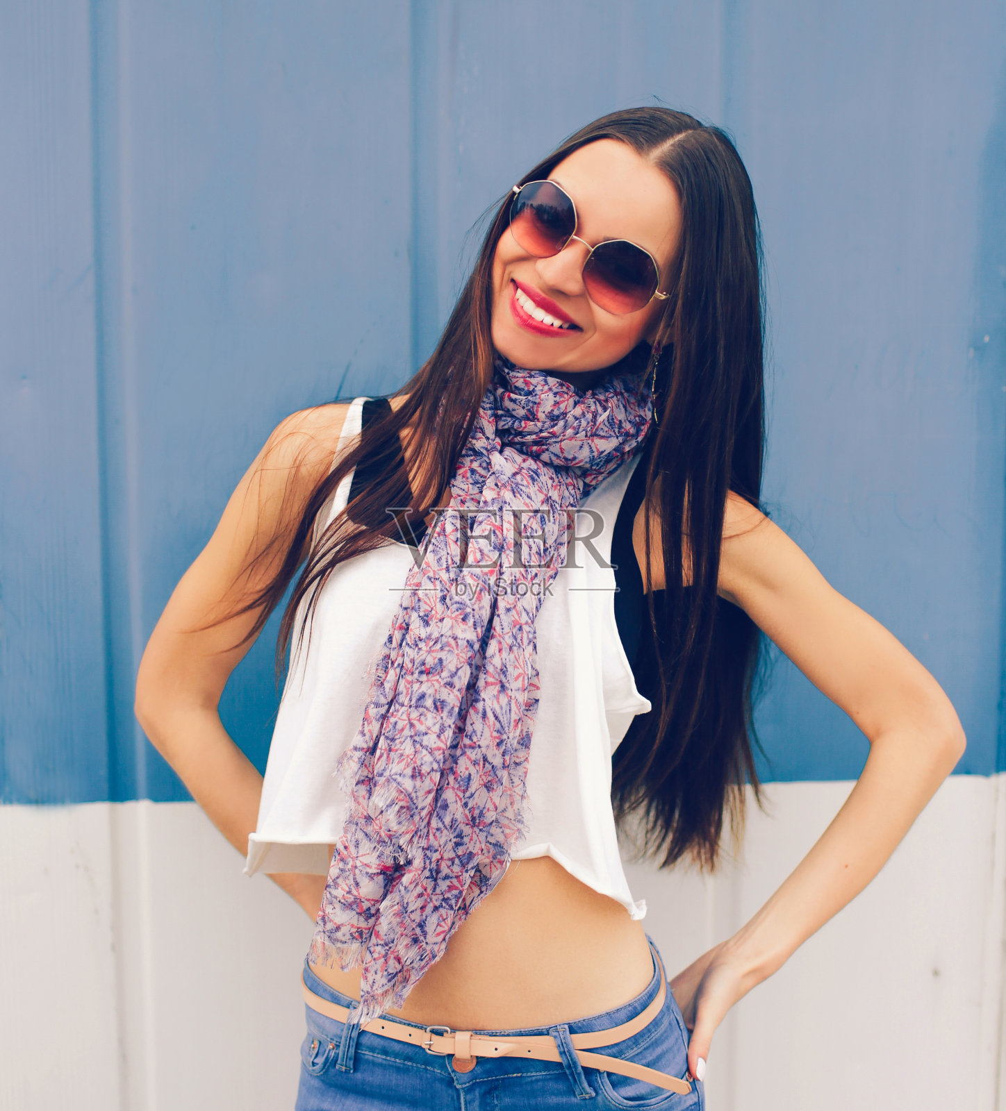 一个时髦的女孩穿着空空的白色t恤和牛仔裤，靠在一堵蓝色的街道墙上摆姿势，这是一个t恤印刷厂的空布局照片摄影图片