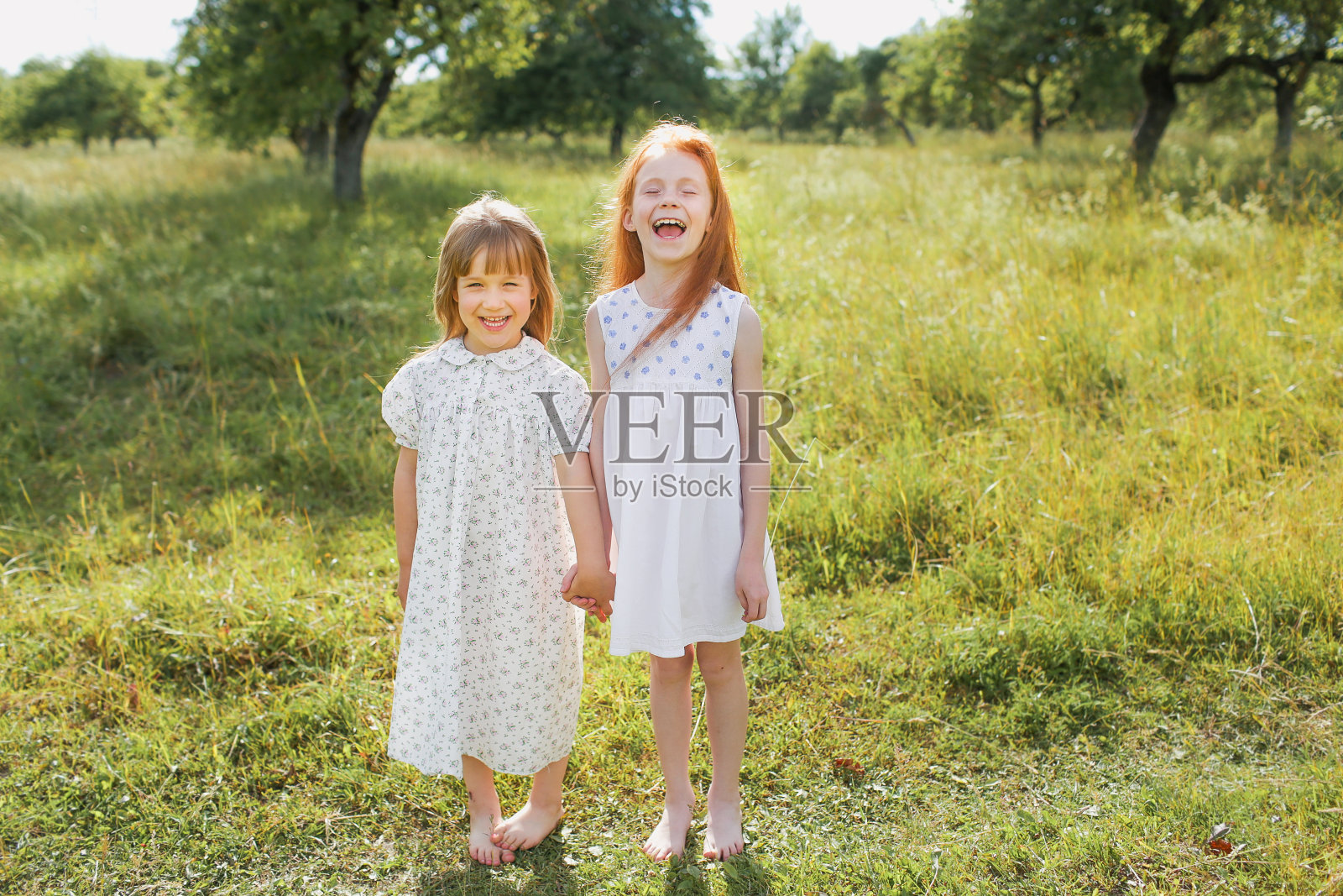 两个小女孩姐妹在草地上玩得很开心，手牵着手穿着轻薄的衣服。夏天，天气晴朗，心情好照片摄影图片