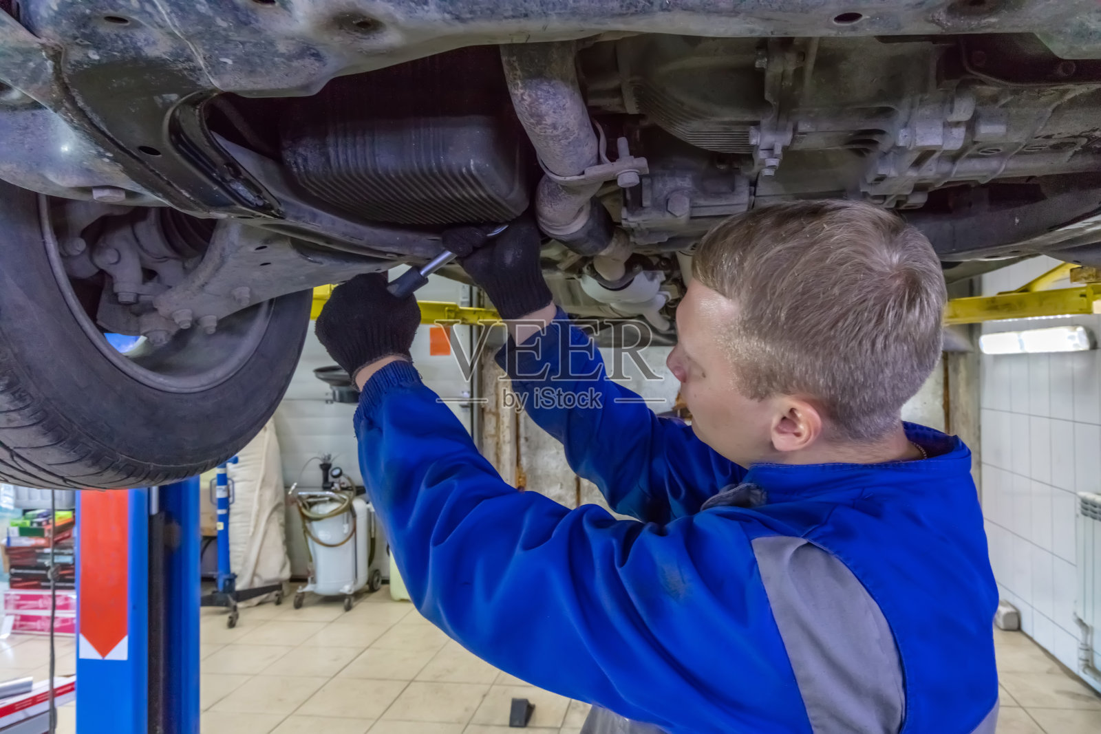 在汽车修理厂修车的技工。技术员穿着蓝色工作服，用扳手。汽车在液压升降机上照片摄影图片