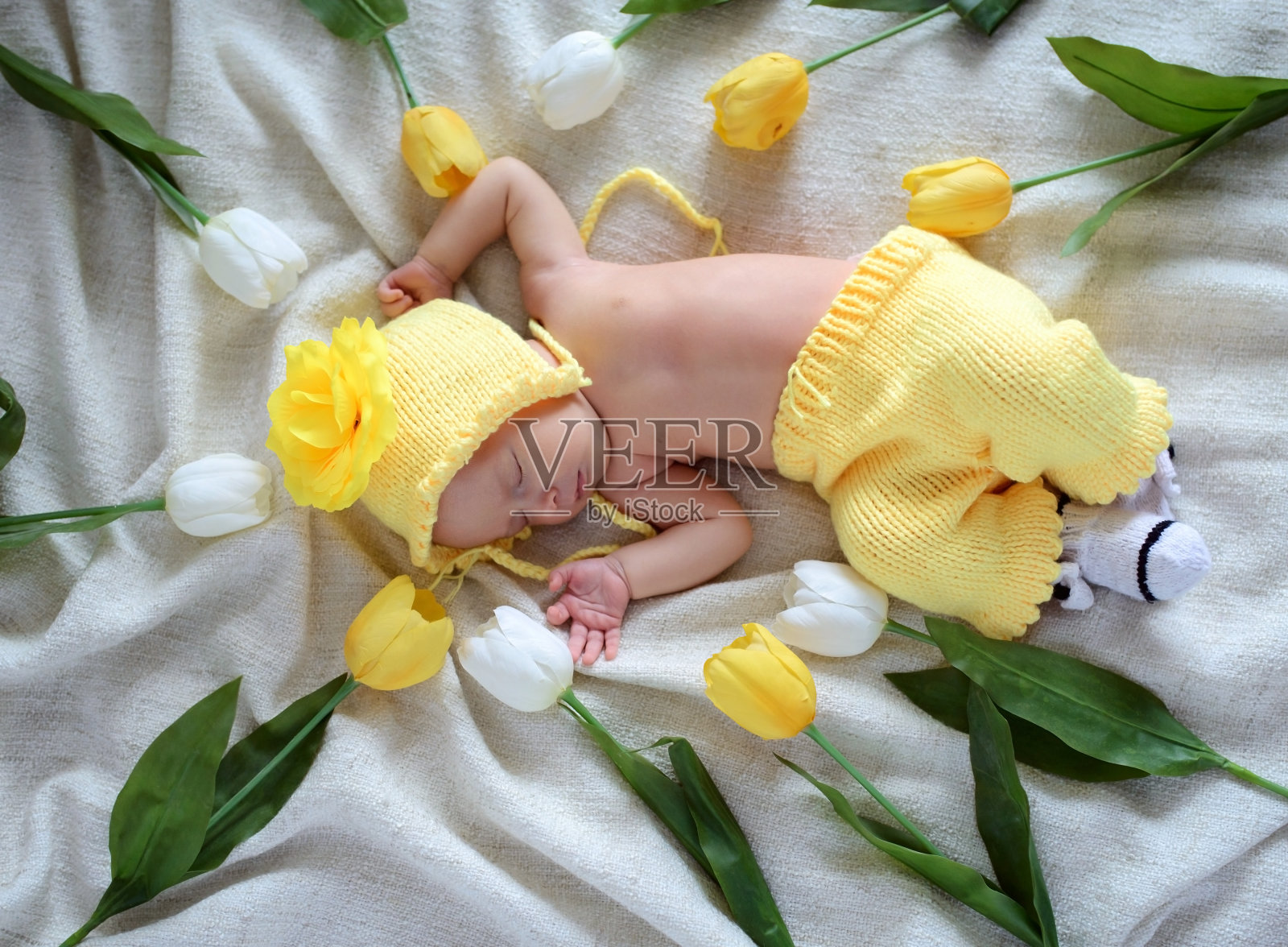 刚出生的小女婴穿着黄色的针织衣服，仰面躺在郁金香花丛中。一个星期大的小孩的美丽肖像。照片摄影图片