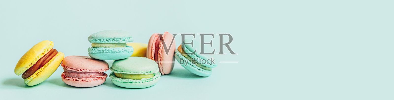 甜杏仁彩色粉蓝色黄绿色马卡龙或马卡龙甜点蛋糕孤立在时尚的蓝色柔和背景。法国甜的饼干。简约的食品烘焙概念。平躺俯视图，横幅照片摄影图片