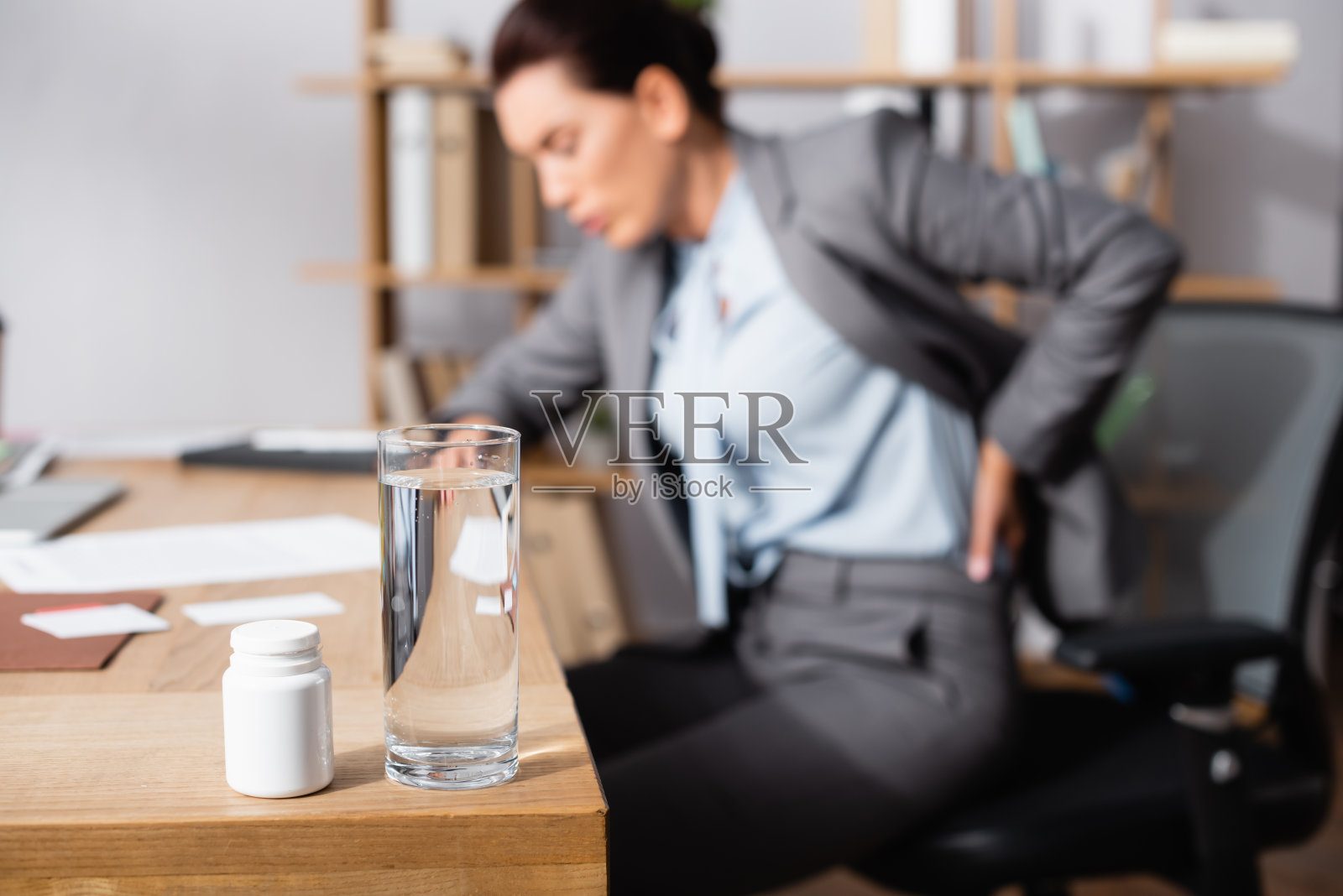 桌上放着一杯水和药物，背景是受伤的女商人照片摄影图片
