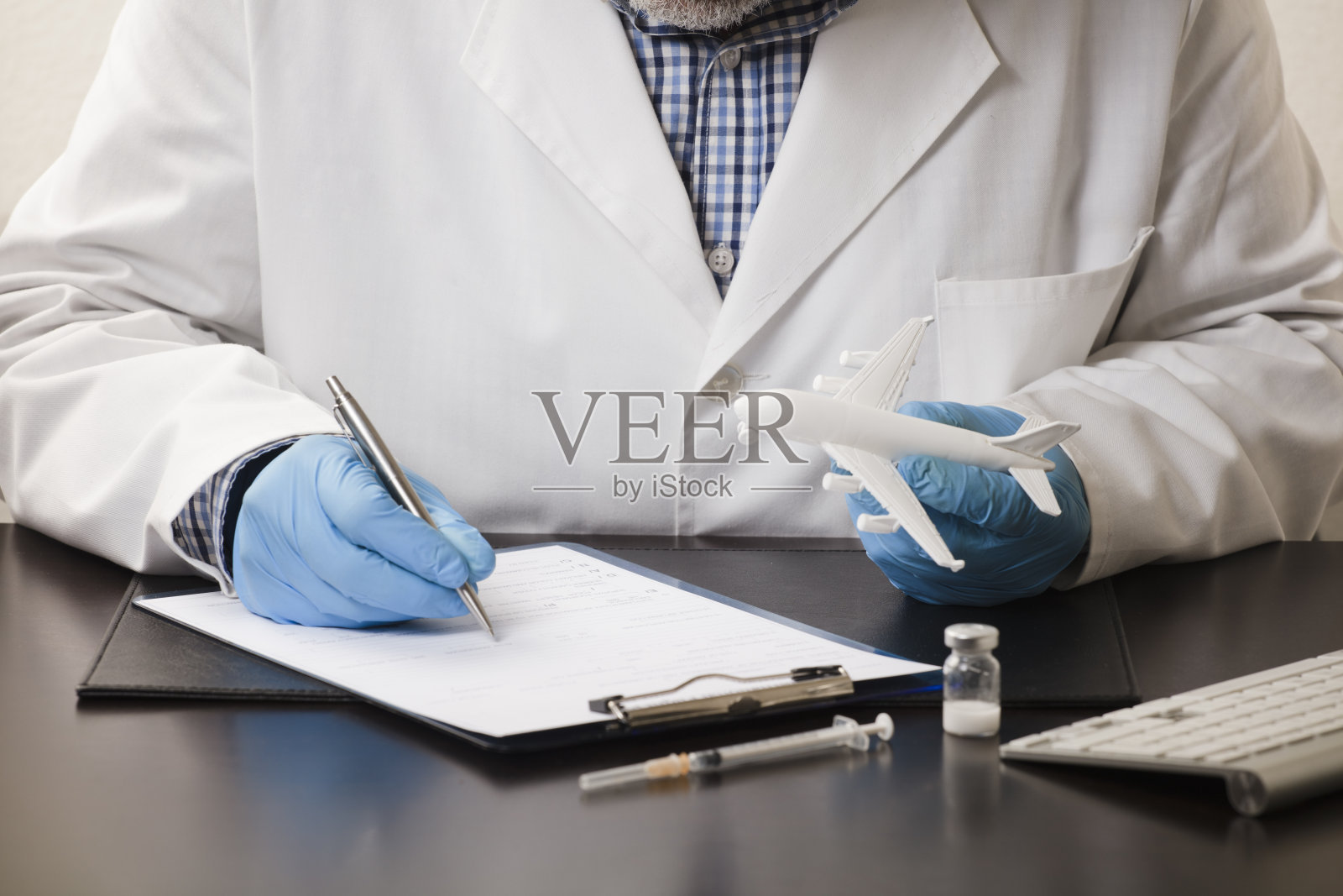 医生的手用笔填写数据，在表格上，用白色的平面，注射器，电脑键盘，在工作台上，白色的背景。照片摄影图片